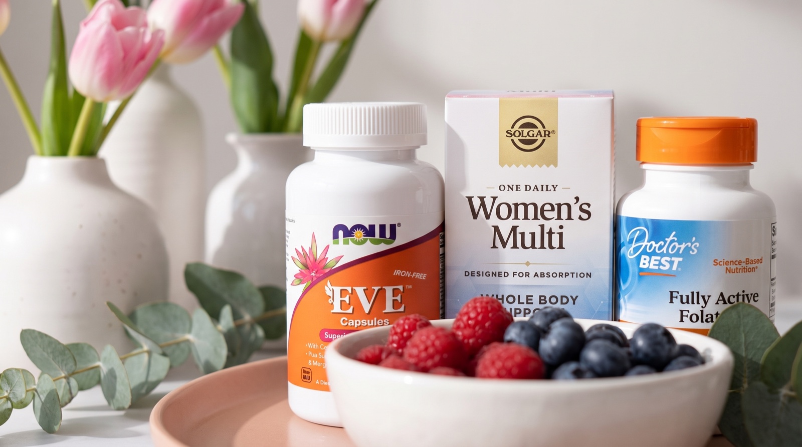 Мультивитамины Eve NOW Foods, Women’s Multi Solgar и фолат Doctor’s Best рядом с тюльпанами и ягодами