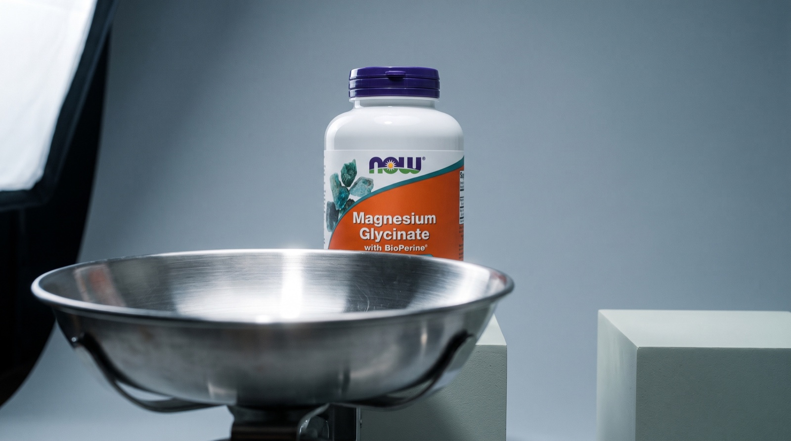 Глицинат магния NOW Foods в студии на подиуме рядом с чашей весов